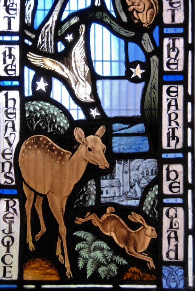 A stained glass window depicting a deer and other woodland creatures