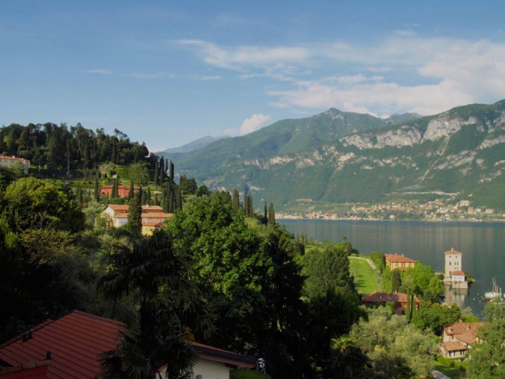 A vibrant green cliffside dotted with houses, sloping down to Lake Como