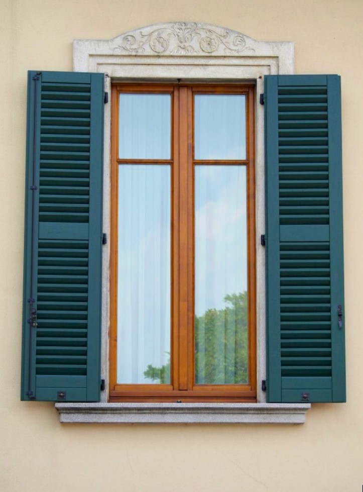A tall, narrow window with blue shutters set in a beige stone wall