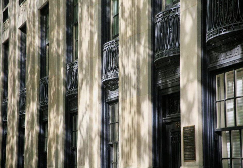 A sandstone building dappled with sunlight and shadows cast by surrounding trees