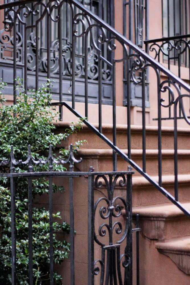 A side view of a staircase of brownstone walkup, with an ornate, wrought iron railing