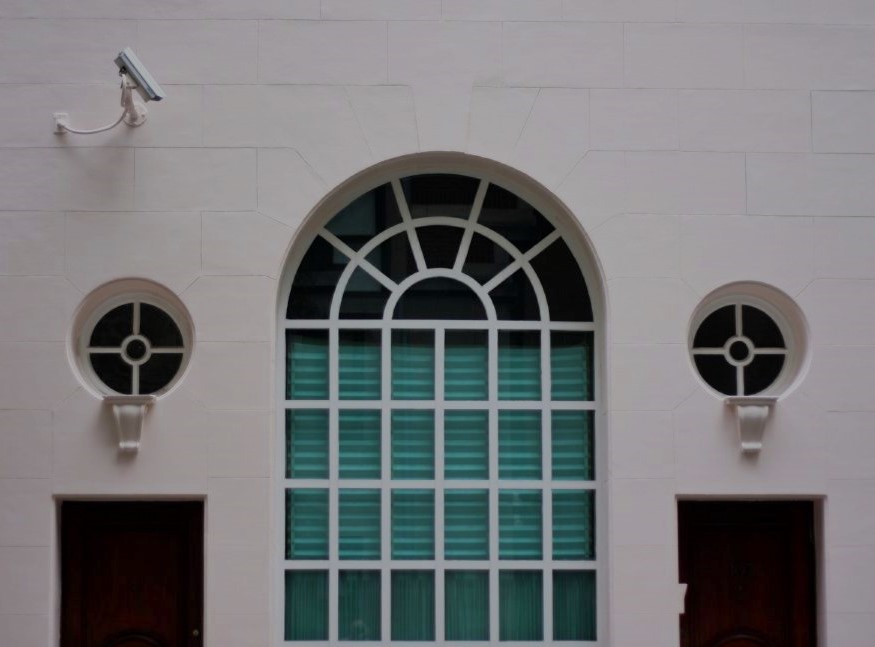 Three ornate windows set in a white wall, two of which are small and round, flanking the larger centre window, which is arched at the top